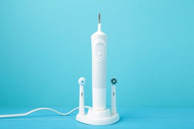 Mavi arka planda şarj aleti olan modern elektrikli diş fırçası. Üst görünüm