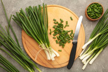 Gri beton arka planda kesme tahtasındaki taze yeşil soğanlar. Üst görünüm