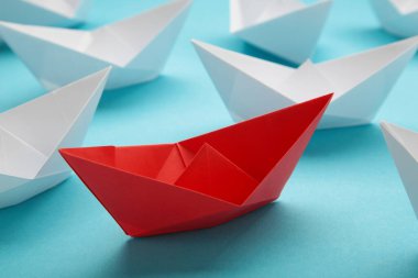 Liderlik kavramı. Kırmızı lider kağıt gemi mavi arka planda beyazlar arasında yol alıyor. Mesaj için yer var. Üst görünüm