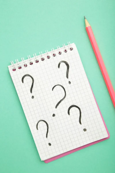 Question mark symbol on white paper with pencil on mint background, top view. Vertical photo