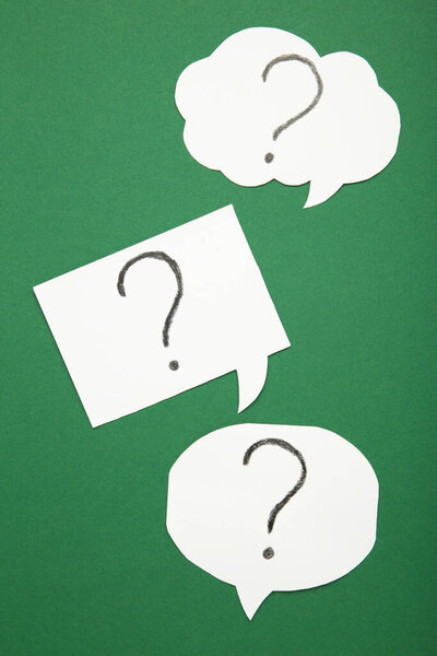 Question marks on white stickers on green background. Top view.
