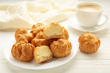 Kremalı ev yapımı profiteroller ve beyaz arka planda bir fincan kahve. Taze pişmiş altın profiterol. Üst görünüm.