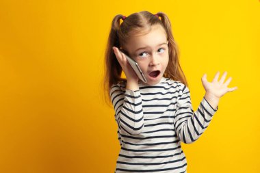 Sarı arka planda cep telefonuyla konuşan komik küçük kız. Üst görünüm