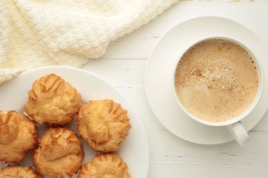 Kremalı ev yapımı profiteroller ve beyaz arka planda bir fincan kahve. Taze pişmiş altın profiterol. Üst görünüm.