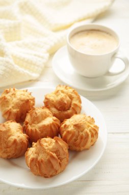 Kremalı ev yapımı profiteroller ve beyaz arka planda bir fincan kahve. Taze pişmiş altın profiterol. Üst görünüm.