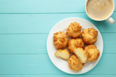 Kremalı ev yapımı profiteroller ve mavi ahşap arka planda bir fincan kahve. Taze pişmiş altın profiterol. Üst görünüm.