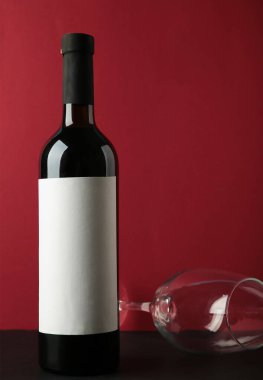 Kırmızı şarap şişesi ve koyu kırmızı arka planda şarap kadehi. Dikey fotoğraf. Üst görünüm