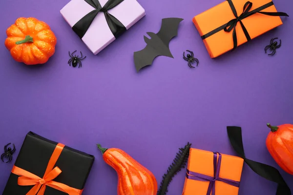 Happy Halloween holiday concept. Flat lay gift boxes, orange pumpkins, bats, spiders on violet background. Halloween greeting card template. Top view