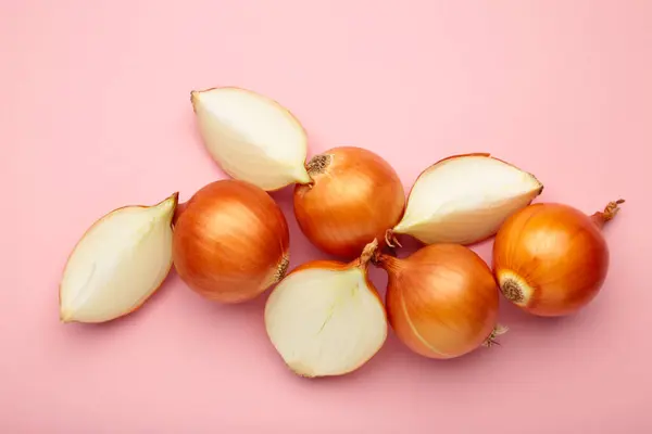 Fresh healthy onions and sliced onion on pink background. Top view