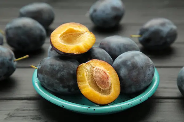 Stock image Fresh plums on blue plate on black wooden background. Top view