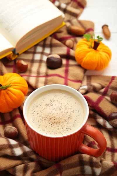 A cup of coffee with autumn decoration and book on blanket. Cozy home, autumn concept. Vertical photo