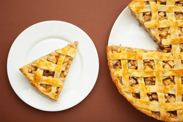 Apple pie and piece of pie on brown background. Copy space. Top view