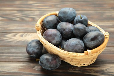 Kahverengi ahşap zemin üzerinde bir sepet taze olgun erik. Üst görünüm