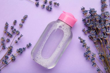 Mor zemin üzerinde Micellar temizleyici su ve lavanta, üst görünüm.