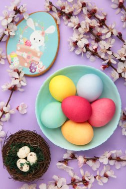 Paskalya zencefilli ekmeği ve mor arka planda mevsimlik çiçekli yumurtalar. Tatlı Paskalya konsepti, tebrik kartı. Dikey fotoğraf