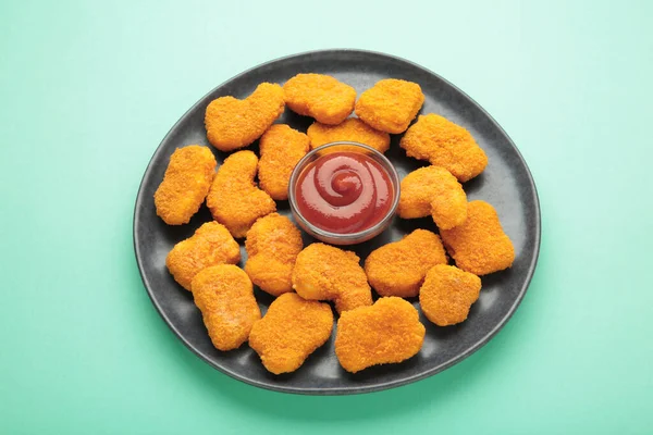 Chicken nuggets with ketchup on plate on mint background. Top view
