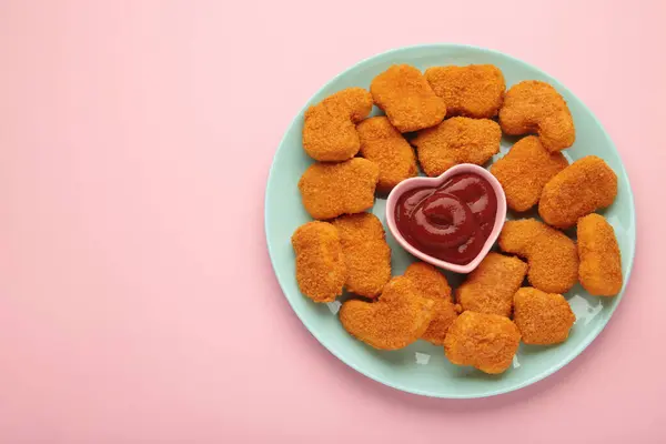 Chicken nuggets with ketchup on plate on pink background. Top view