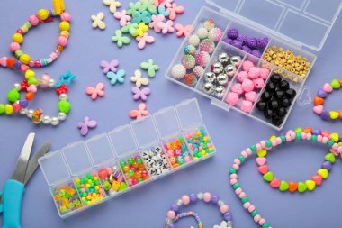 Mor arka planda çocuk için el yapımı mücevherler yapmak için boncuklu bir kutu. Bileklik. El yapımı aksesuarlar. Üst görünüm