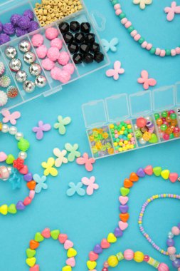 Mavi arka planda çocuk için el yapımı mücevher yapmak için boncuklu bir kutu. Bileklik. El yapımı aksesuarlar. Üst görünüm