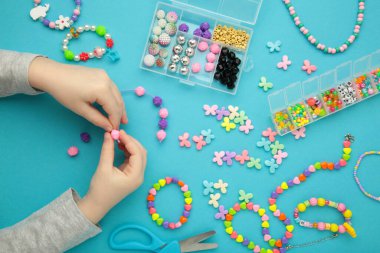 Küçük kız mavi arka planda bilezikler yapmış. El yapımı boncuklu mücevherler. Kolyeler ve bilezikler çok renkli boncuklar ve incilerden yapılmış. Bilezik boncukları..