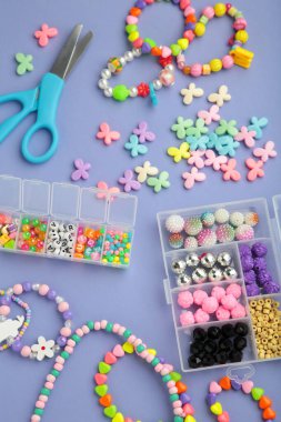 Mor arka planda çocuk için el yapımı mücevherler yapmak için boncuklu bir kutu. Bileklik. El yapımı aksesuarlar. Üst görünüm