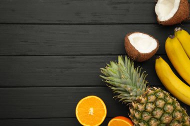 Tropik meyveler. Ananas, hindistan cevizi, portakal ve muz, siyah arka planda. Üst görünüm