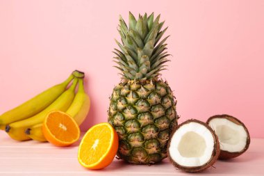 Tropik meyveler. Ananas, hindistan cevizi, portakal ve muz pembe arka planda. Üst görünüm