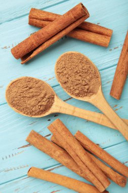 Tarçın çubukları ve tahta kaşıkta toz mavi ahşap arka planda. Üst görünüm