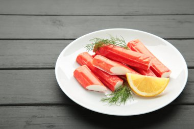 Lezzetli, taze yengeç çubukları ve siyah ahşap arka planda bir dilim limon. Üst görünüm