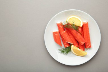 Lezzetli, gri arka planda bir dilim limon dilimli taze yengeç çubukları. Üst görünüm