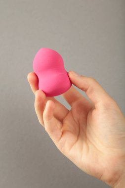 Gri arka planda pembe makyaj süngeri olan bir kadın eli. Üst görünüm