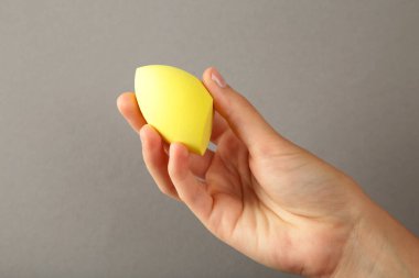 Gri arka planda sarı makyaj süngeri olan kadın eli. Üst görünüm