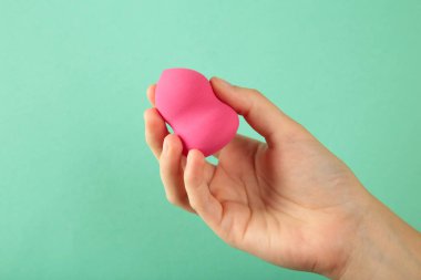 Arka planda pembe makyaj süngeri olan bir kadın eli. Üst görünüm