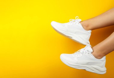 Sarı arka planda şık beyaz ayakkabılı kadın bacakları. Mesaj için yer var. Üst görünüm