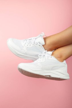 Pembe arka planda şık beyaz ayakkabılı kadın bacakları. Mesaj için yer var. Üst görünüm