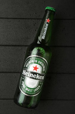 Mykolaiv, UKRAINE - Temmuz 2024: Siyah ahşap arka planda bir şişe Heineken Lager Birası.