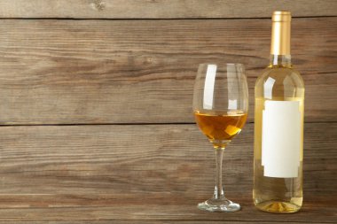 Gri ahşap arka planda duran yarım boş şarap kadehiyle etiketlenmemiş beyaz şarap şişesi..