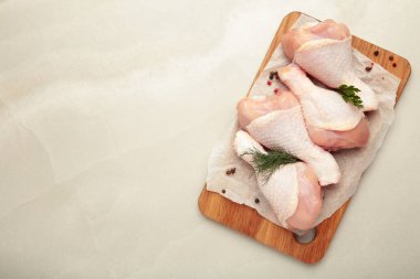 Hafif arka planda kesme tahtasına baharat konmuş çiğ tavuk budu..