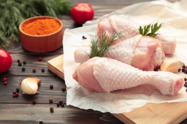 Kahverengi arka planda kesme tahtasına baharat konmuş çiğ tavuk budu..