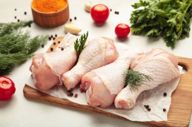 Hafif arka planda kesme tahtasına baharat konmuş çiğ tavuk budu..