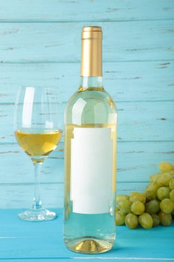 Mavi ahşap arka planda üzümlü beyaz şarap şişesi ve cam. Üst görünüm