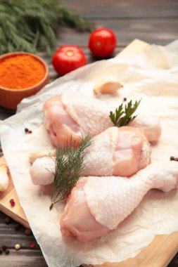 Kahverengi arka planda kesme tahtasına baharat konmuş çiğ tavuk budu..