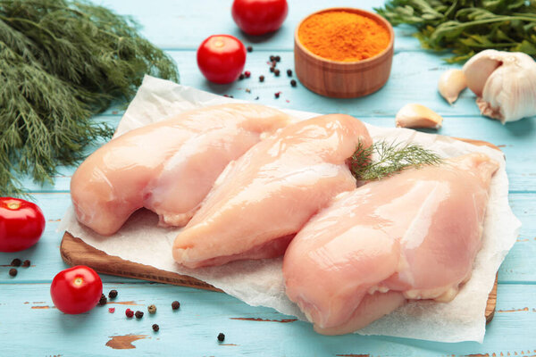Raw chicken fillet on a cutting board with tomato, spices and dill on blue wooden background.