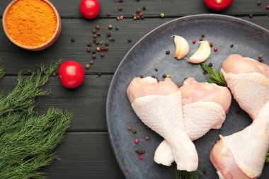 Siyah ahşap arka planda siyah tabakta baharatlı çiğ tavuk budu. Üst görünüm.