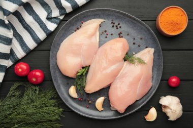 Tabakta çiğ tavuk filetosu, domates, baharat ve siyah arka planda dereotu..