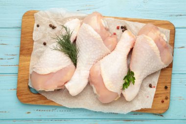 Mavi arka planda kesilmiş tahtada baharatlı çiğ tavuk budu..