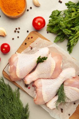 Hafif arka planda kesme tahtasına baharat konmuş çiğ tavuk budu..