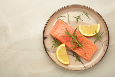 Kırmızı balık. Biberiyeli çiğ somon filetosu ve gri arka planda bej tabakta limon. Üst görünüm