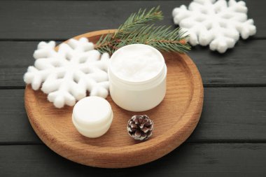 Kartaneli kavanoz kozmetik ürünleri ve siyah ahşap arka planda köknar ağacı dalları..