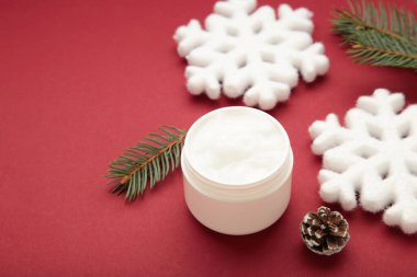 Kartaneli kavanoz kozmetik ürünleri ve kırmızı arkaplanda köknar ağacı dalları.